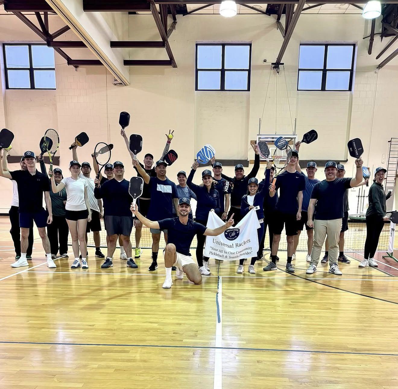 The Universal Rackets coaching team with paddles and racquets raised behind the company banner